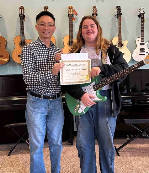 November Student of the Month, Paige, standing with her teacher, Mr. Linden, holding her certificate and new electric guitar. 